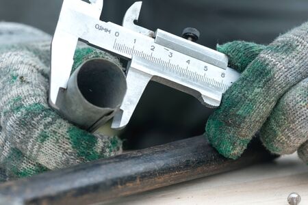 Worker is holding in hands a metal part and is measuring a diameter by a calipers.の写真素材
