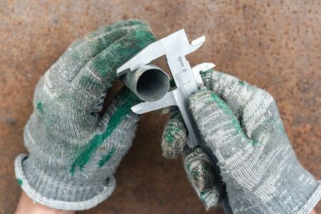 Worker is holding in hands a metal part and is measuring a diameter by a calipers.