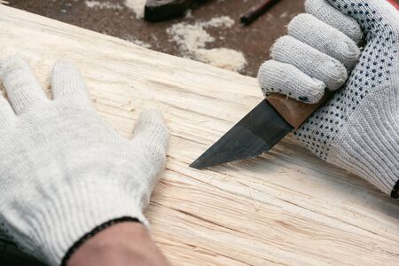 Carpenter is decorating and make a texture on a wooden board with a deep groove by a knife on his workbench.の写真素材