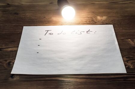 To do list paper page on the wooden desk table surface in the light of bulb lamp with copy space. To...