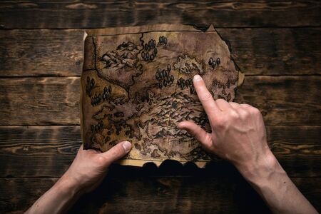 Old map in man adventurer hands on a brown table background. Treasure hunt concept.