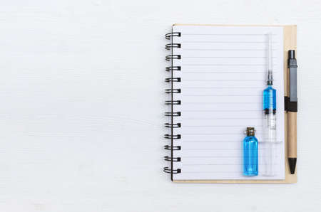 Syringe, blank page notepad and ampoule with blue liquid medicine on the doctor table. Medical journal or doctor prescription mockup.の写真素材