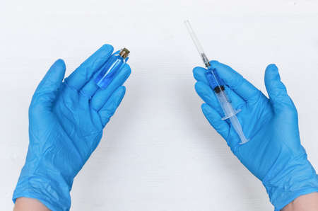 Nurse is holding in hand a syringe with blue liquid medicine on the doctor table background.