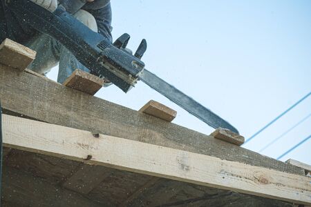Worker is cutting a wood by a chainsaw.