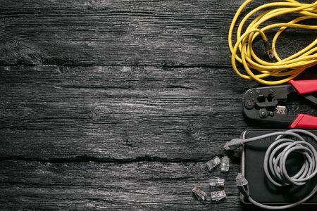 Computer network laying concept. Crimper tool, utp cable, net switch and connectors on black wooden...
