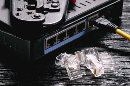 Computer network laying concept. Crimper tool, utp cable, net switch and connectors closeup on black...