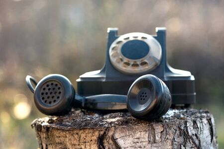 Black old phone on a wooden log on the street background.の写真素材