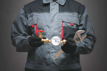 Plumber is holding in hands a water meter and adjustable wrench close up.の写真素材