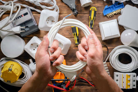 Electrician is holding in hands a wiring on wooden workbench with various electrical equipment background.の写真素材