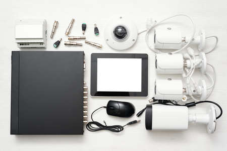 Digital tablet with blank screen, video recorder and various security cameras on the white flat lay table background.の写真素材