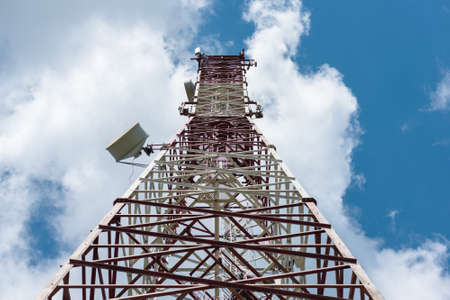 Cell tower with antennas on a blue sky background.