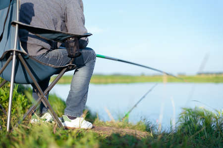 Fisherman sits on a chair by the lake and fishes.の写真素材