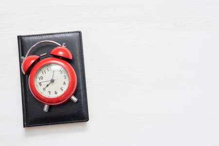 Black leather book and red alarm clock ont he white table background with copy space.の写真素材
