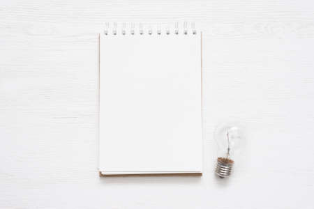 Notepad with blank pages and a lightbulb on the white wooden table background. Ideas list template.の写真素材