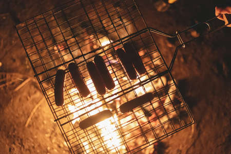 Grill with sausages on the coals of campfire.の写真素材