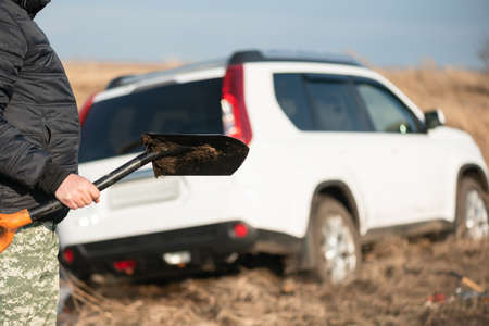 Driver with a shovel in hands and suv stuck in the swamp.の写真素材