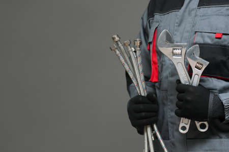 Plumber with adjustable wrenches and water hoses on a gray background with copy space.