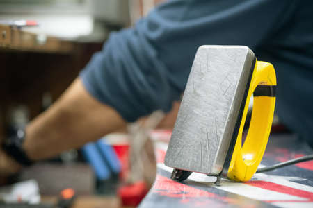 Wax iron on the damaged snowboard surface close up.の写真素材
