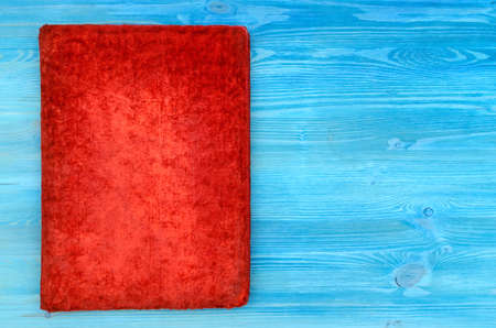 Closed red vintage book with suede cover isolated on blue wooden table surface background. Education...