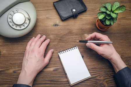 Telephone in male businessman hands and notebook with copy space on office table. Contact us. Business conversation.の写真素材
