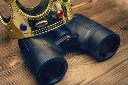VIP premium search. Binoculars and golden crown on wooden desk table background. In searhing for something special.の写真素材