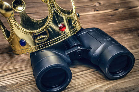 VIP premium search. Binoculars and golden crown on wooden desk table background. In searhing for something special.の写真素材