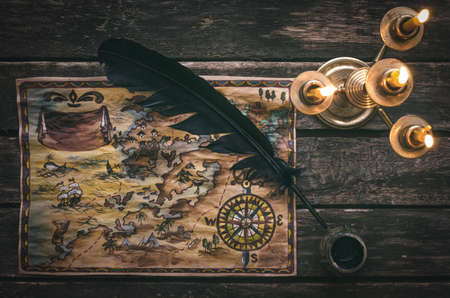 Pirate treasure map, burning candle, feather pen and inkwell on wooden ship table background.の写真素材
