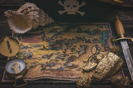 Pirate treasure map, gold nuggets, dagger and pirate hat on aged wooden table background. Sea travel.の写真素材