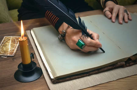 Tarot cards on fortune teller desk table. Future reading. Woman witch writes by feather pen a magic...