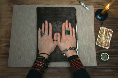 Book of magic. Tarot cards on fortune teller desk table. Future reading. Woman witch reads a ancient magic scroll book with copy space and learn art of prediction on wooden table.の写真素材