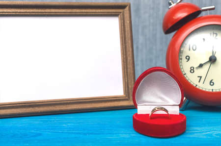 Wedding ring in a gift present box and empty photo frame of a loved one copy space and red alarm...