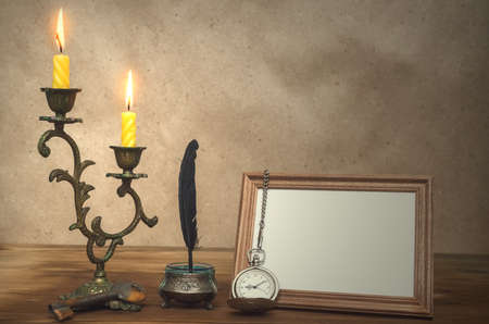 Empty photo frame with copy space burning candle in vintage candlestick and feather pen with inkpot...