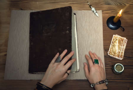 Book of magic with mystical light. Tarot cards on fortune teller desk table. Future reading. Woman witch open ancient magic scroll book and learn art of prediction on wooden table.の写真素材