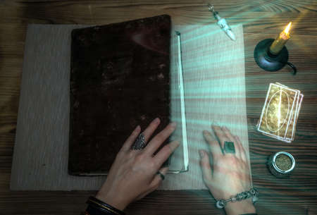 Book of magic with mystical light. Tarot cards on fortune teller desk table. Future reading. Woman...