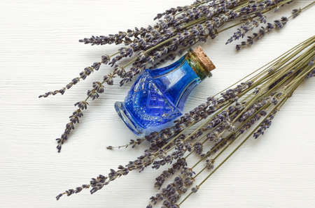 Dry lavender branches and bottle with blue medical tincture on white wooden background. Herbal medicine concept. Alternative medicine.の写真素材