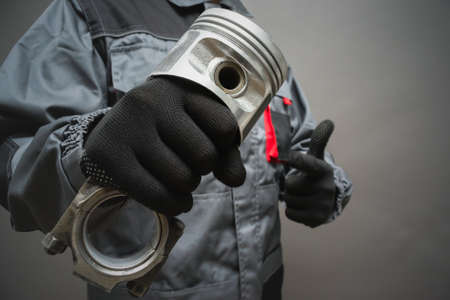 A car mechanic is holding and old car engine piston close up on gray background.の写真素材