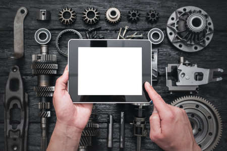 Car service worker is holding a blank screen digital tablet above spare parts background. Car spare...