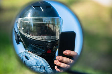 Motor biker reflection in the mirror which is using a mobile phone close up.の写真素材
