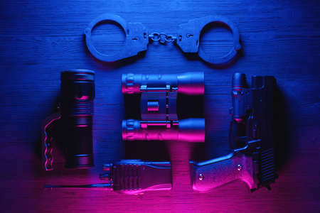Spy secret service agent desk table concept background. Gun, radio, binoculars, handcuffs and flashlight on the neon background.の写真素材