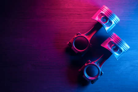Old car engine pistons with connecting rod on the car service workbench background in the neon...