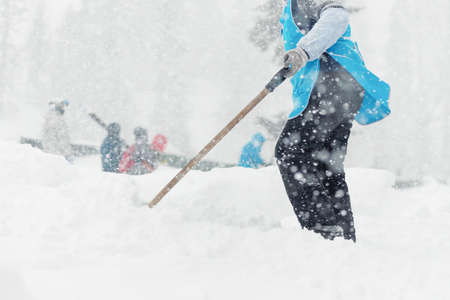 Woman is cleaning the snow by the spade in the blizzard close up.