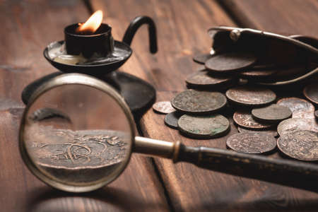 Old ancient coins and magnifying glass on the brown wooden table backgroundの写真素材