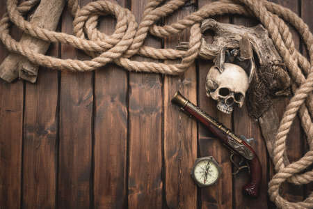 Pirate table concept background with copy space. Human skull, musket gun, mooring rope and compass on the table.の写真素材