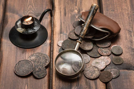 Old ancient coins and magnifying glass on the brown wooden table backgroundの写真素材