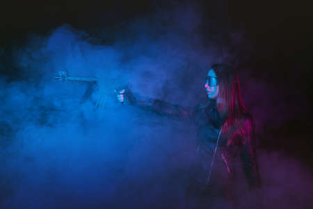Futuristic girl soldier with a gun in the smoke on the dark background.の写真素材