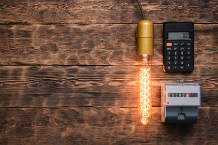 Calculator, light bulb and electric meter on the wall. Calculation of electricity costs concept.の写真素材