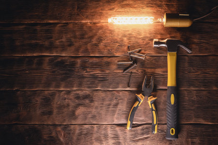 Hammer, pliers and nails in the light of lamp on the wooden workbench background top view.の写真素材