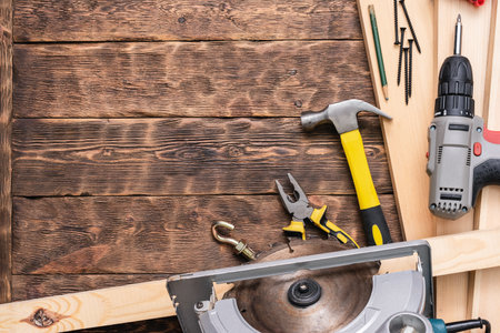 Circular saw, hammer, pliers and wooden bars on the brown wooden workbench background with copy...