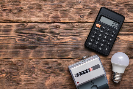 Calculator, light bulb and electric meter on the wall. Calculation of electricity costs concept.の写真素材