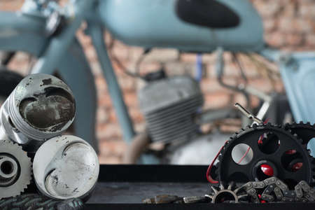 Motorcycle repairing service concept background. A car engine piston, gear and wrenches on the rack on the old garage background.の写真素材
